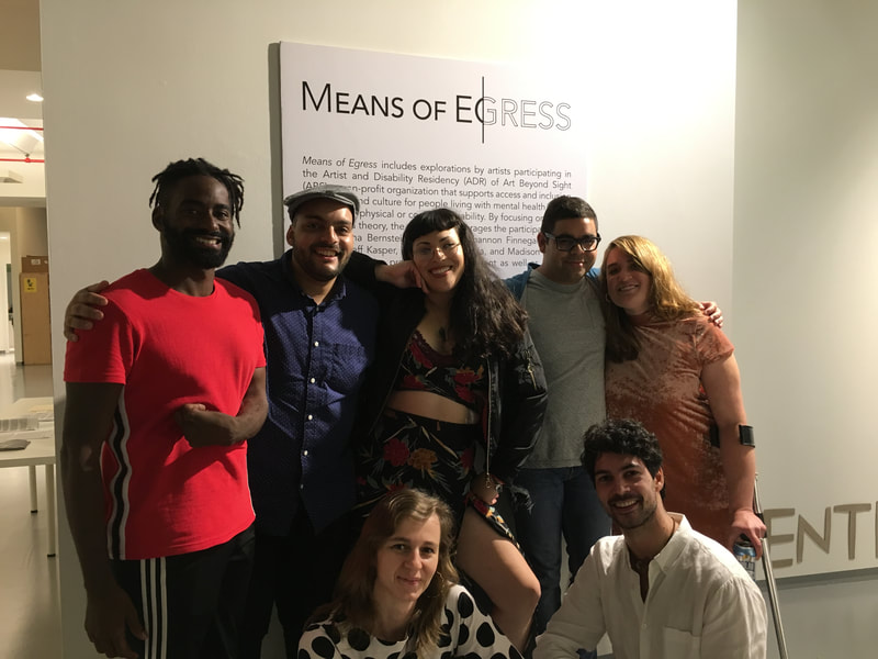 Seven  disabled artists in Art and Disability Residency standing in front of the intro text to Means of Egress exhibition at Dedalus Foundation. Standing and smiling from left to right are Jerron Herman, Jeff Kasper, Jordana Bernstein, Kevin Quiles Bonilla, Madison Zalopany, and crouching in front of them is Shannon Finnegan and myself.